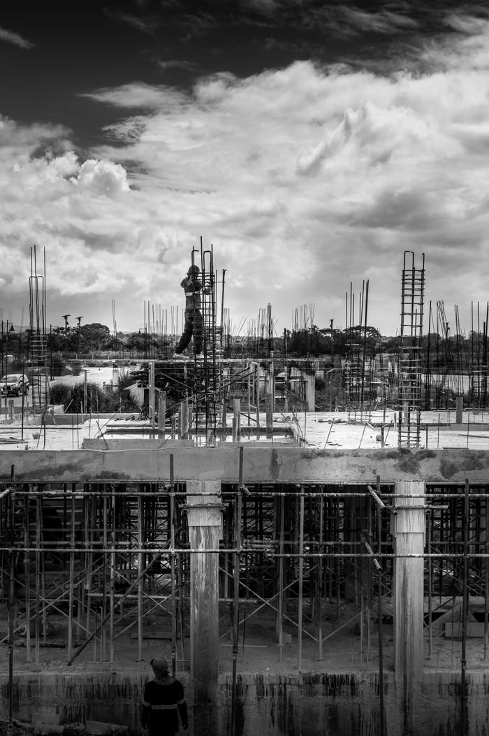 A construction worker standing on scaffolding at an outdoor building site, captured in black and white.