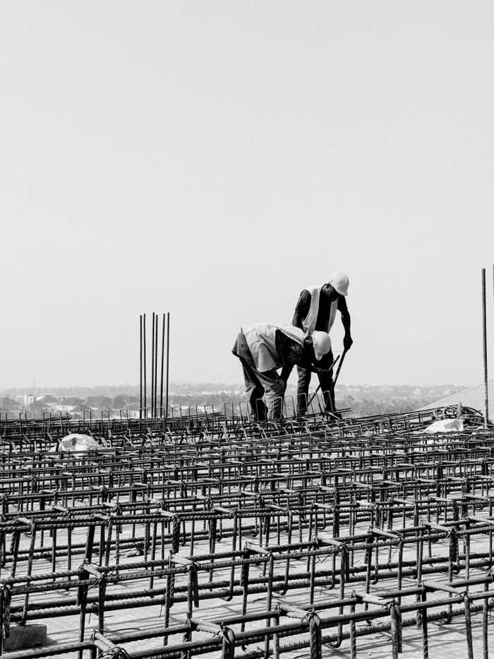 Monochrome image of two workers on a construction site with rebar detailing.